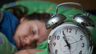 Eine Frau schläft, während ein Wecker neben ihr auf dem Nachttisch steht. Das eigene Schlafverhalten lässt sich laut einer Studie trainieren – ein Stück weit.