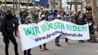 Teilnehmer der Demonstration von Gegnern der Corona-Maßnahmen in Hamburg halten ein Transparent mit der Aufschrift „Wir müssen reden!“.