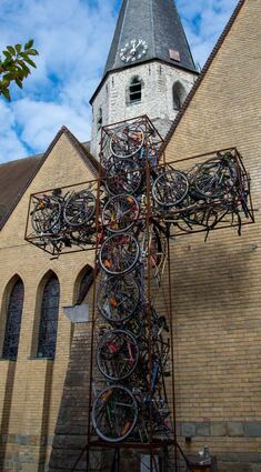 Ein mehrere Meter hohes Kreuz aus alten Fahrrädern (l.) ist vor der Kirche St. Amadeus im Stadtzentrum von Zwevegem zu sehen. Durch ein Bullauge kann man Innere des 15 Meter hohen Tauchturms blicken (r.o.). Große Figuren am Straßenrand machen auf Zebrastreifen aufmerksam (r.u.).
