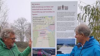Reimund Strauch von Mensch vor Verkehr (l.) und Bürgermeister Helmut Glanzner zeigen anhand der neu aufgestellten Hinweistafel die Dimensionen der geplanten Bahn-Neubaustrecke östlich von Einhausen.