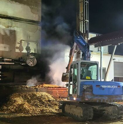Nach ersten Löscharbeiten wurden die qualmenden Hackschnitzel mit Hilfe eines Baggers auf den Betonboden geschaufelt und abgelöscht.