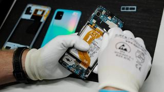 Der Mitarbeiter einer Werkstatt repariert ein Smartphone. Verbraucher müssen dafür oft tief in die Tasche greifen.