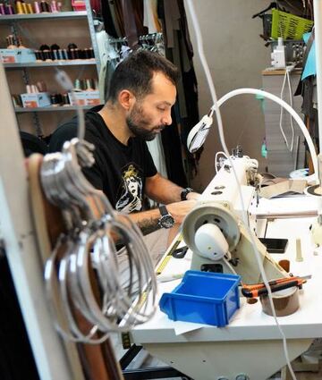 Meysam Dadashnejad sitzt an der Nähmaschine und produziert Lederhalsbänder – und Sancho, der Hund einer Mitarbeiterin, dient als Model.