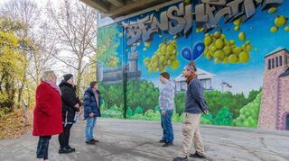 Die sanierte Brücke der Saarstraße schmückt sich jetzt mit einem Bensheim-Graffiti. Julian Hauser und Sven Düfer (v.r.) haben das Streetart-Werk auf dem Widerlager an der Lahnstraße geschaffen. Erste Stadträtin Nicole Rauber-Jung, Bauingenieurin Katharina Handel und KMB-Geschäftsführer Frank Daum machten sich am Montag ein Bild von dem fertigen Kunstwerk.