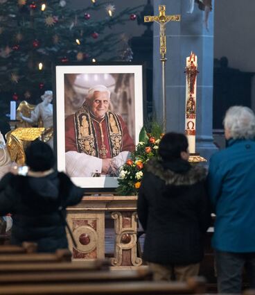 Menschen stehen am Neujahrstag in einer Kirche in Altötting vor einem Bild des verstorbenen emeritierten Papstes Benedikt XVI.