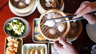 Ein Mann greift mit Essstäbchen nach Dim sum, gedämpften Teigtaschen, in einem Bambuskorb.