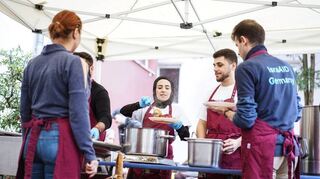 Teilnehmende der „Brückenbau“-Gruppe helfen bei der Essensausgabe in der Ada-Kantine in Frankfurt-Bockenheim.