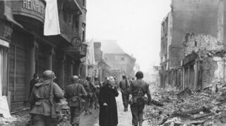 Das berühmte Bild zeigt die 64-jährige Anna Mix, geborene Hesch, die 1945 fassungslos auf die Trümmer des zerstörten Hauses ihrer Schwester Margaretha Hesch blickt, während die US-Truppen durch Bensheim marschieren.