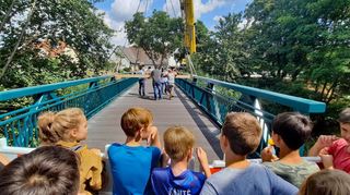 Kinder aus dem Ort und Schüler der benachbarten Grundschule verfolgten gebannt, wie der vier Meter breite Steg über dem Fluss passgenau montiert wurde.