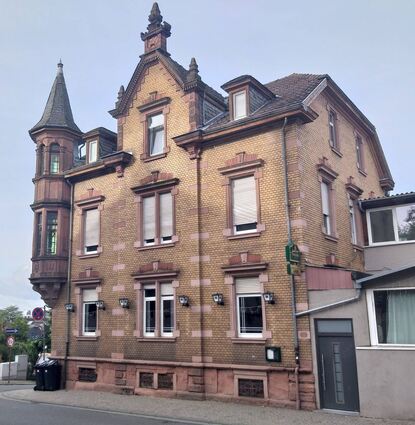 An der Ecke der Darmstädter Straße zur Friedrichstraße fällt ein aufwändiger Erkerturm mit farbiger Verglasung ins Auge. Gleichzeitig ist das Haus, zu dem er gehört, eher schlicht gestaltet.