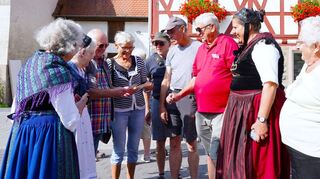 Die Gruppe macht Station in Elmshausen, wird dort von Ortsvorsteher Walter Kirschbaum, Frauen der Trachtengruppe Reichenbach und Einwohnern von Elmshausen begrüßt, im Gespräch mit einigen der Reisenden werden Familienbilder betrachtet.