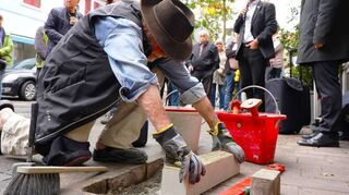 Heimat- und Kulturvereinsvorsitzender Thilo Figaj (r.) und Bürgermeister Schönung übernahmen die Ansprachen, Künstler Gunter Demnig setzte die Stolperschwelle, die mit einem längeren Messingband versehen ist, über die Synagoge informiert.