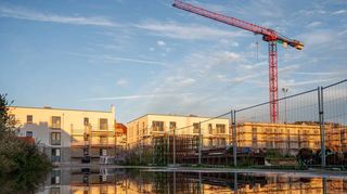Die Neubauten auf dem ehemaligen Meerbachsportplatz spiegeln sich in der Abendsonne in einer Pfütze auf der Baustelle. Die CDU-Fraktion hat sich bei einem Ortstermin über den Baufortschritt informiert.