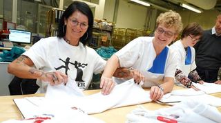 Dentsply Sirona-Mitarbeiterin Britta Pfeifer (l.) ließ sich in der bhb-Wäscherei zeigen, wie man Poloshirts schnell und ordentlich faltet. bhb-Geschäftsführer Christian Dreiss (r.) erläuterte die Hintergründe zur Aktion „Schichtwechsel“.
