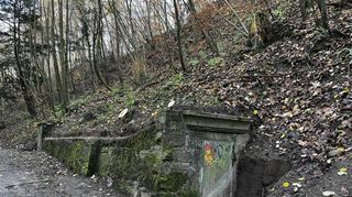Die Brunnenhäuser fallen stilistisch und von ihrer Größe her sehr unterschiedlich aus. Inzwischen halb im Hang versunken ist der Eingang mit dem einst schmückend profilierten Sturz.