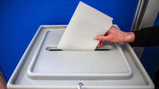 Eine Frau wirft einen Stimmzettel in eine Wahlurne.