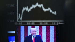 Hinter einem Fernsehmonitor, auf dem US-Präsident Donald Trump zu sehen ist, zeigt die Anzeigetafel mit der Dax-Kurve fallende Kurse.