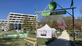 Das Bündnis End Cement protestiert mit einem Protestcamp gegen den Großkonzern Heidelberg Materials. Der Firmensitz ist im Hintergrund zu sehen.