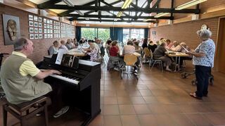 Matthias Arnold am Klavier, während die ehrenamtliche Helferin Hildegard Gottwald mit ihm und den Senioren singt.