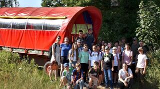 Im Jagdrevier Einhausen-Nord steht die Schülergruppe des AKG Bensheim an einem Planwagen unterhalb eines Hochsitzes, links die Lehrerinnen Sofie Landgraf und Theresa Benner, rechts die Jäger und Laura Armbruster, mit Mütze, bereit für Informationen zum Thema Jagd und Natur.