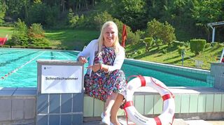 Die hessische Ministerin hat auf dem Beckenkopf des Schwimmbads Platz genommen. Mit der finanziellen Förderung können nun auch die notwendigen Reparaturen bei der Umrandung des Beckens durchgeführt werden.