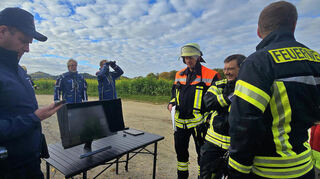 Am Mittershäuser Sportplatz betrachten der Fürther Gemeindebrandinspektor Dominik Bormuth (links), Heppenheims Stadtbrandinspektor Christian Stadler (Dritter von rechts) und Heppenheims Erste Stadträtin Christine Bender (rechts) die Bilder, die via Drohne vom Einsatzort übertragen werden.