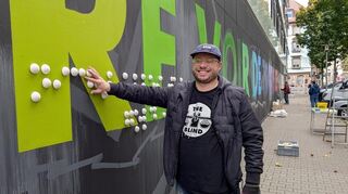Der französische Street-Art-Künstler The Blind ertastet sein Mural in Braille-Schrift in J5.