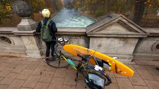 Ein Mann mit einem Surfboard an seinem Fahrrad schaut von einer Brücke auf die - nicht mehr vorhandene - Eisbachwelle im Englischen Garten.